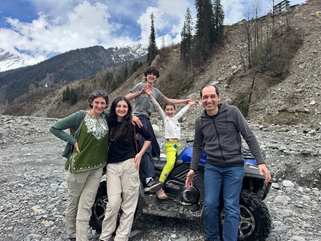 Eve and her family beside an ATV on a rocky riverbed below snowy mountains